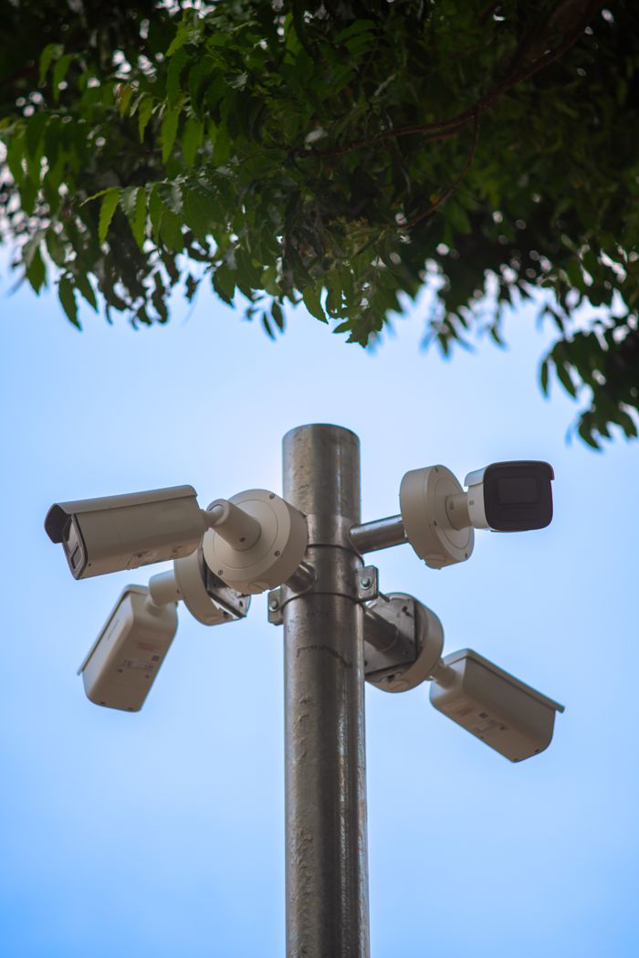 Home Multiple security cameras mounted on a metal pole under a tree, ensuring public safety.