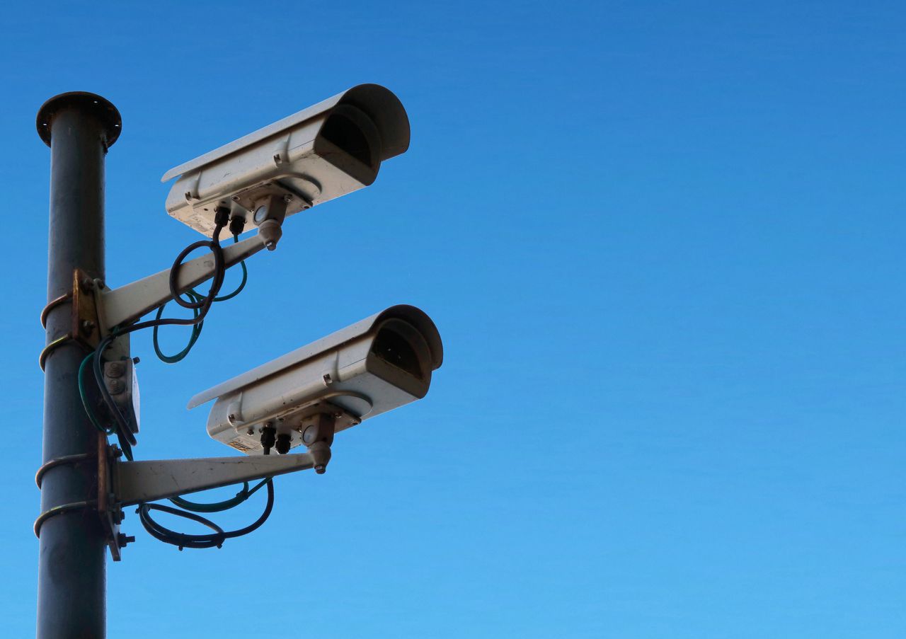 Low angle of security camera attached to black post located isolated on blue sky on sunny day in daytime outside