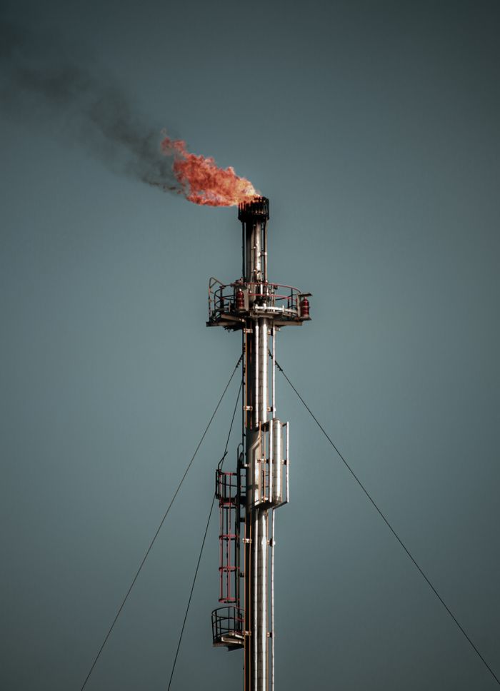 A tall industrial flare stack releasing flame and smoke, set against a clear sky, captures the essence of industrial emissions.